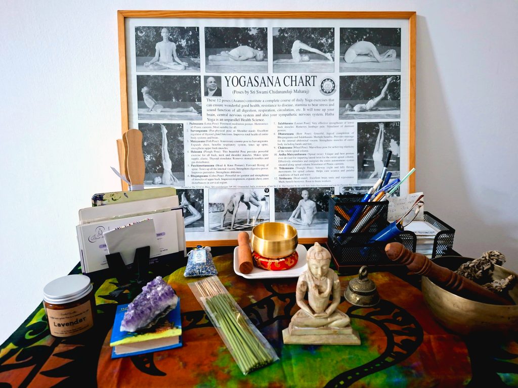 Roi Pajursky - A serene creative workspace and inspiration corner in the artist's studio. The scene features a framed yoga-themed poster, a small golden Buddha statue, incense, and various spiritual artifacts arranged on a desk, creating a mindful atmosphere for artistic creation.